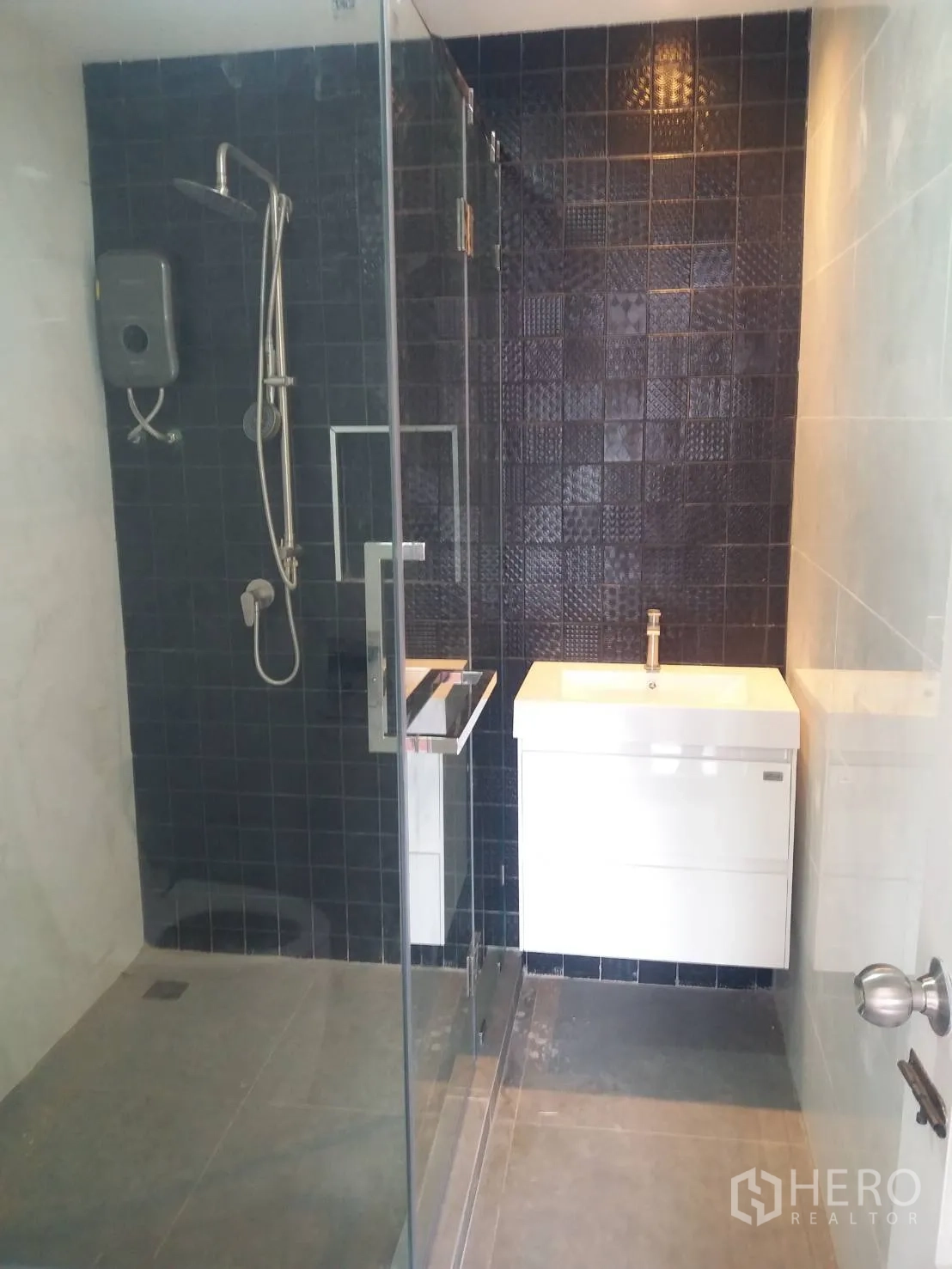 Townhouse for rent in Khlong Toei, Bangkok - Bathroom with glass shower, dark tiled feature wall and a white vanity unit.