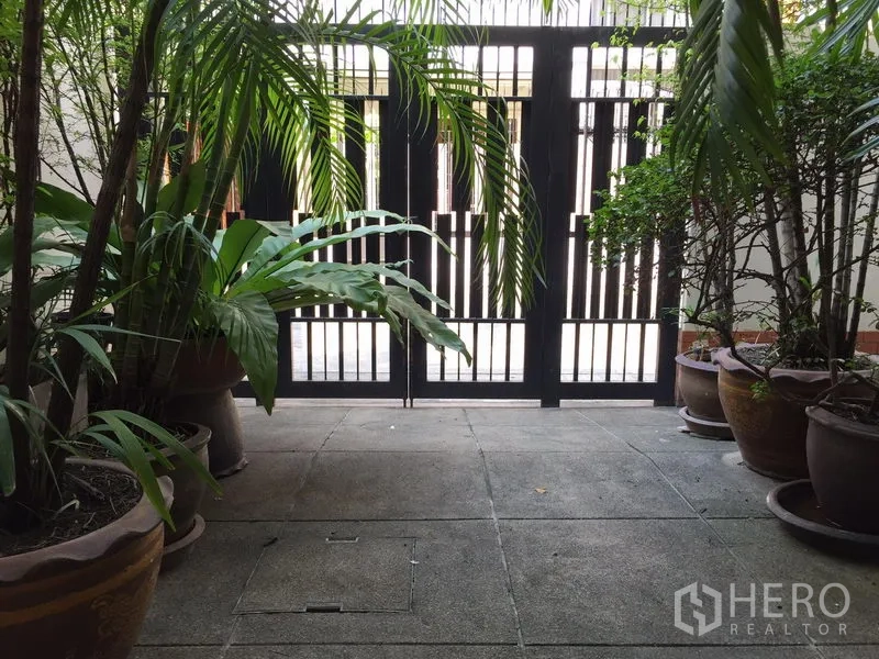 联排别墅 出租在Watthana, Bangkok - 有盆栽热带植物的门前庭院，配黑色金属大门。