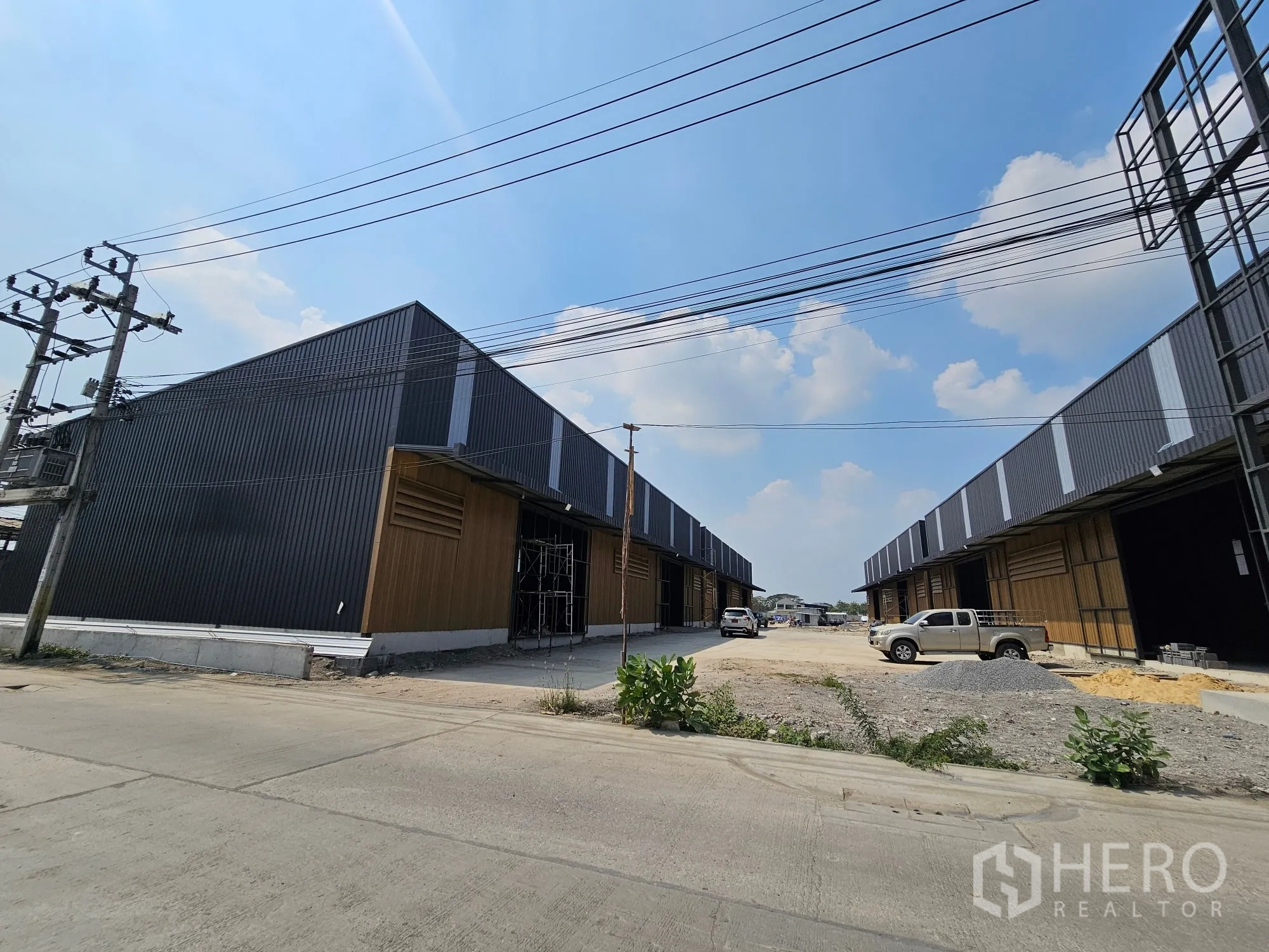 Warehouse for rent in Bang Khen, Bangkok - Newly built warehouse rows with a wide driveway and overhead power lines.