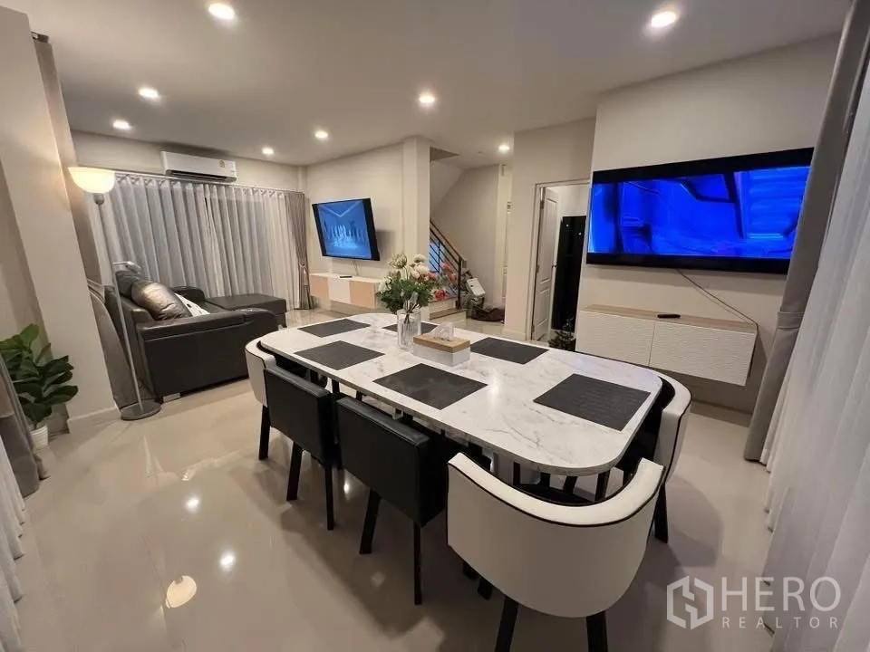 Detached House for rent in Prawet, Bangkok - Open-plan dining area with marble-top table, six chairs and TV feature wall.