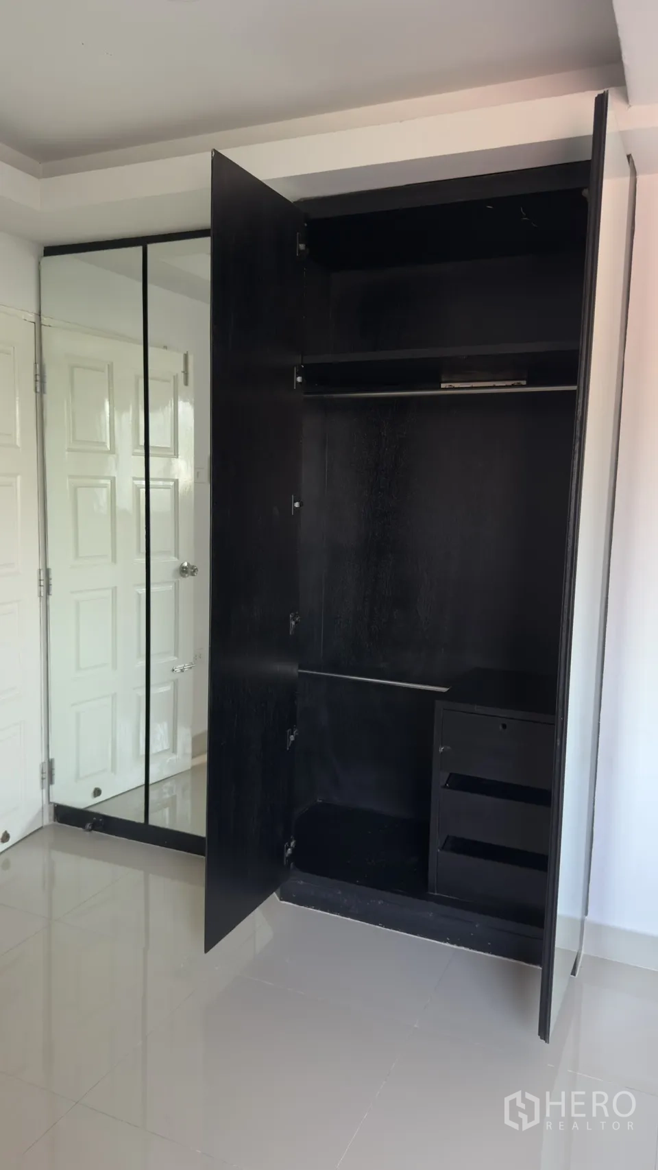 Townhouse for rent in Watthana, Bangkok - Open black wardrobe with hanging space and mirrored doors in a white bedroom.