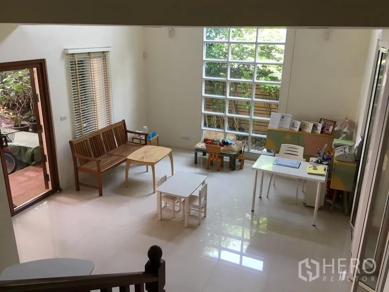 Townhouse for sale in Huai Khwang, Bangkok - Bright ground-floor living area with glossy tiles, large glass-block window and garden access.