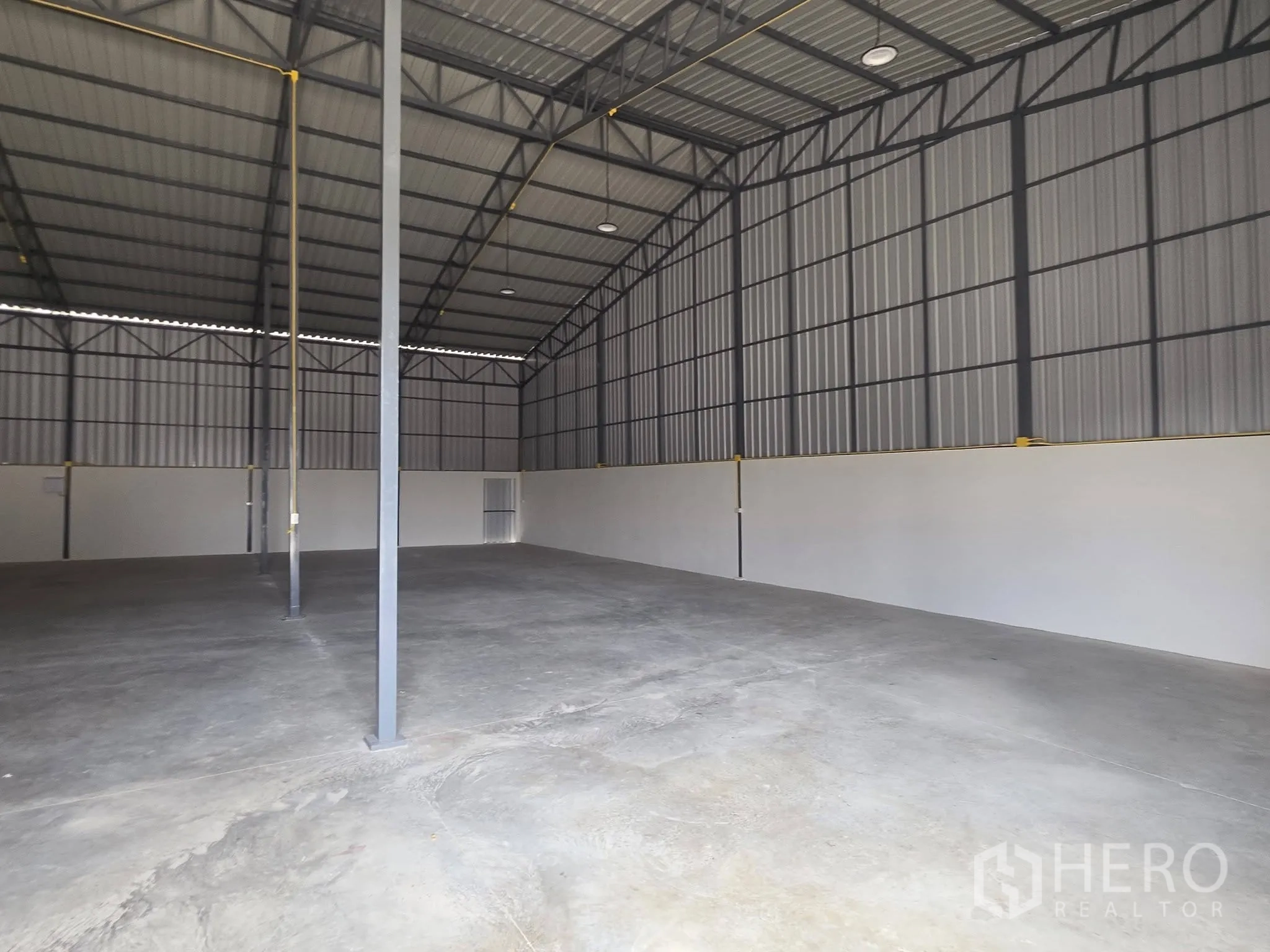 Warehouse for rent in Mueang Samut Prakan, Samut Prakan - Interior of the warehouse showing high roof, steel trusses, columns, and smooth concrete floor.