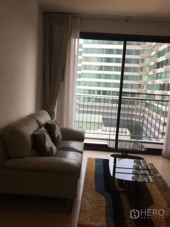 Condominium for rent in Watthana, Bangkok - Living area with sofa and coffee table opening to a balcony via sliding glass doors.