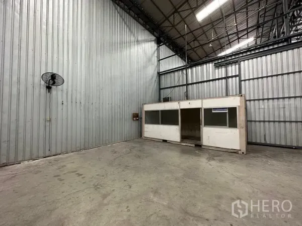 货栈 出租在Pak Kret, Nonthaburi - 仓库一角，墙挂通风扇与内部小型办公室箱体。