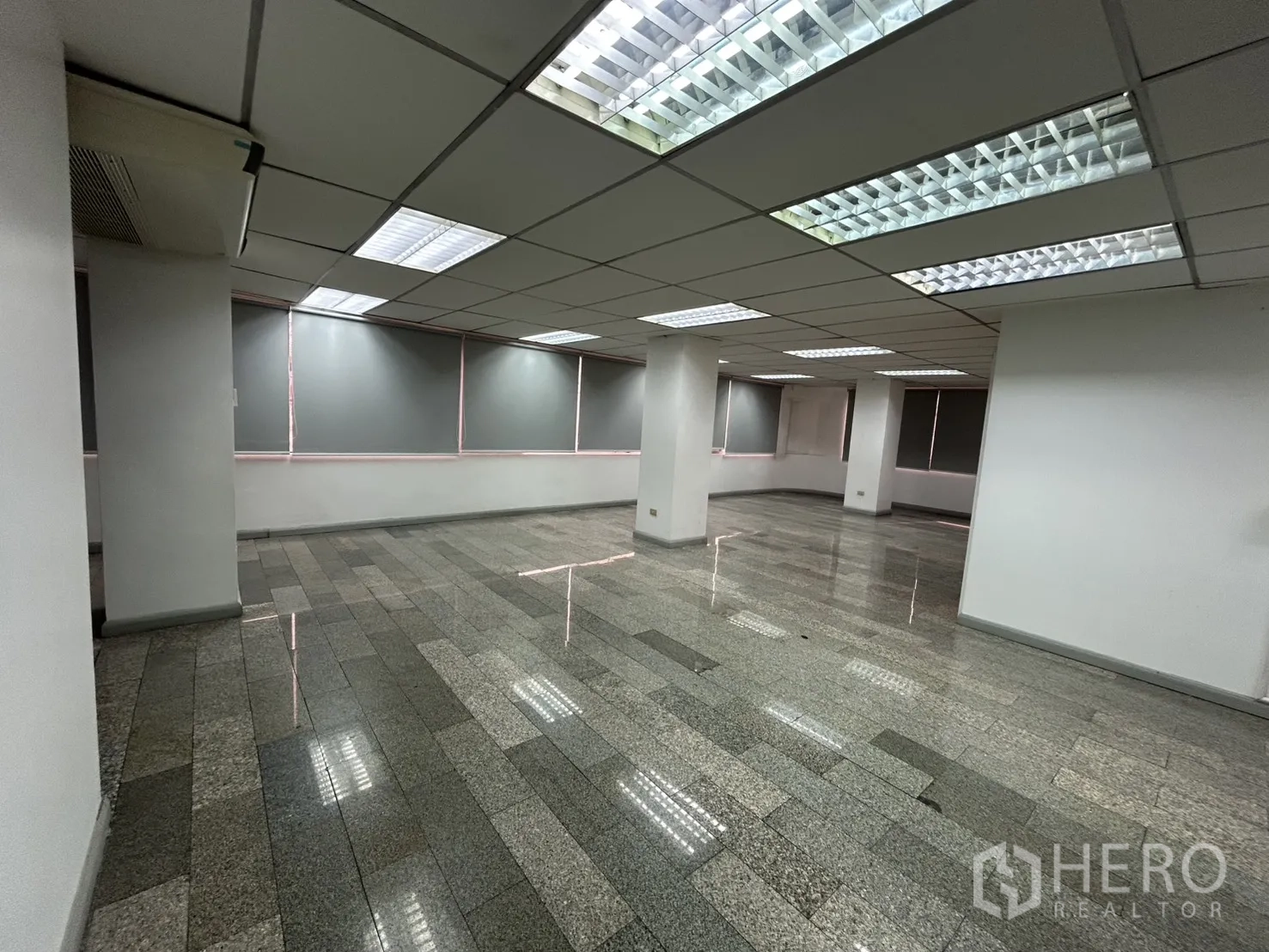 Office Space for rent in Khlong Toei, Bangkok - Large office floor with columns, tiled flooring, roller blinds, and bright ceiling lighting.