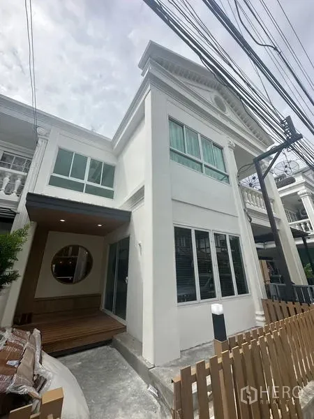 Home Office for rent in Khlong Toei, Bangkok - Contemporary white townhouse facade with tall windows, a small front deck and a wooden picket fence.
