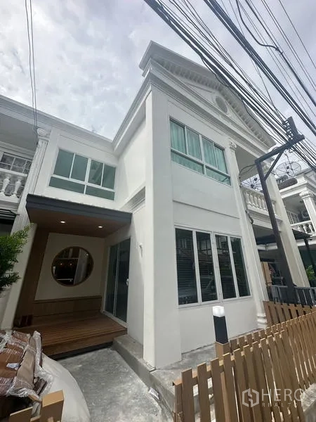 Home Office for rent in Khlong Toei, Bangkok - Contemporary white townhouse facade with tall windows, a small front deck and a wooden picket fence.