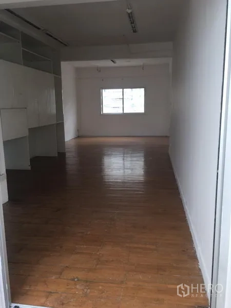 Shophouse for rent in Khlong Toei, Bangkok - Deep shophouse floor with built-in white shelving and a rear window providing daylight.
