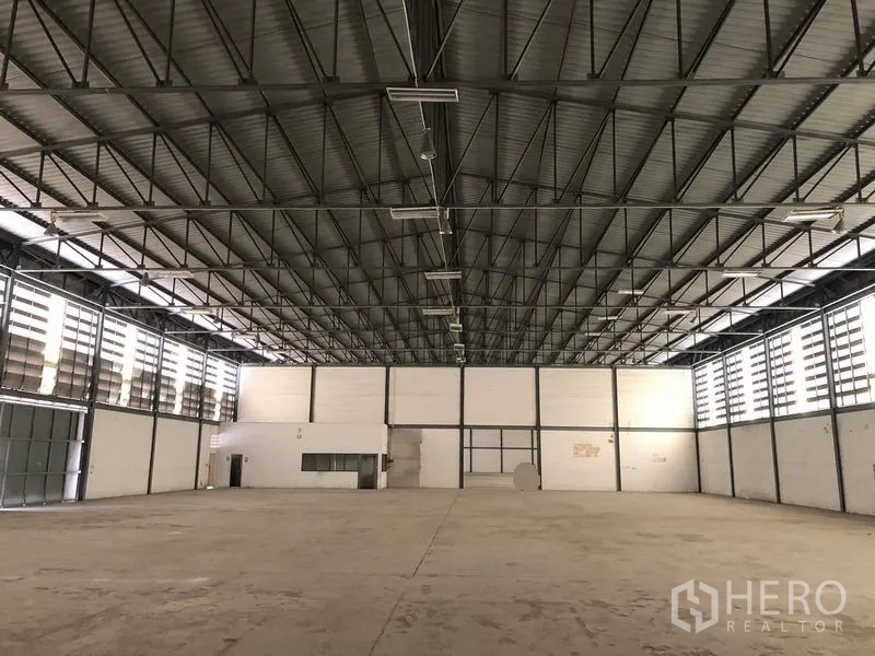 Warehouse for rent in Khlong Luang, Pathum Thani - Spacious warehouse interior with high steel truss ceiling, louvered ventilation and a small office corner.