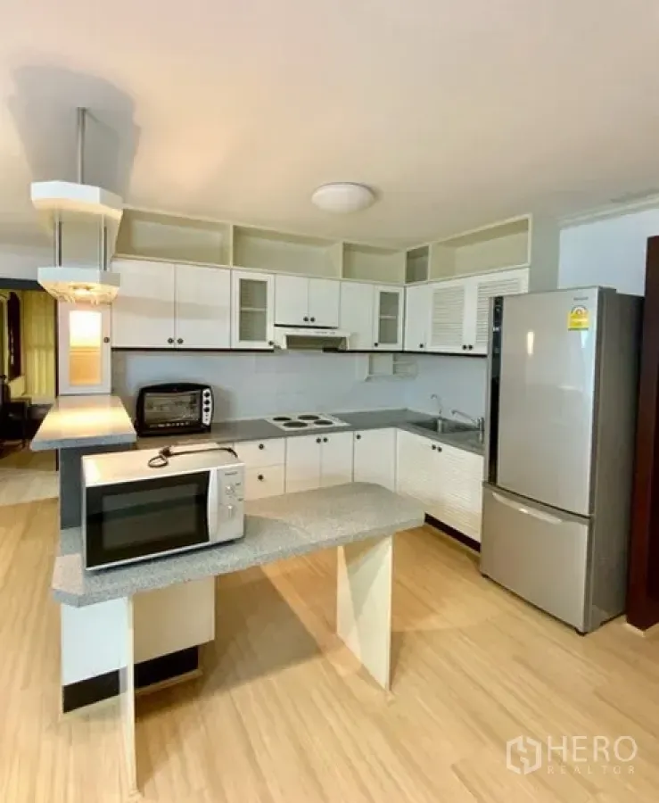Condominium for rent or sale in Watthana, Bangkok - Fitted kitchen with white cabinetry, electric hob, hood, refrigerator and microwave.