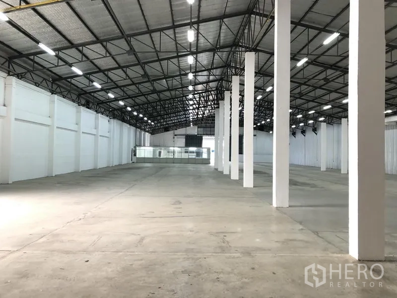 Warehouse for rent in Nonthaburi - Long central aisle of the warehouse showing rows of columns, insulated roof panels and bright white perimeter walls.