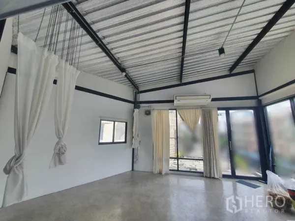 Retail Space for rent in Sathon, Bangkok - Bright open-plan retail studio with high metal ceiling, exposed beams, air conditioner, and sliding glass doors with curtains.