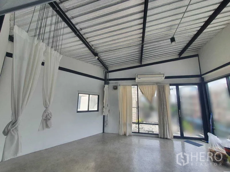 Retail Space for rent in Sathon, Bangkok - Bright open-plan retail studio with high metal ceiling, exposed beams, air conditioner, and sliding glass doors with curtains.