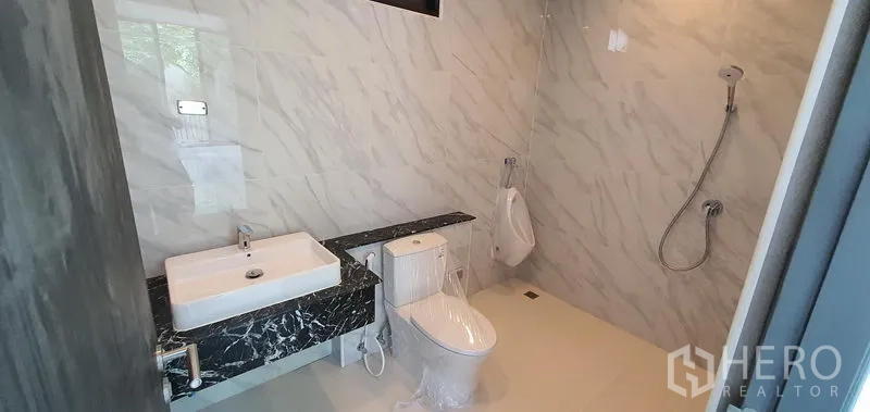 Home Office for rent or sale in Watthana, Bangkok - Marble‑tiled bathroom with shower, toilet, and rectangular basin.