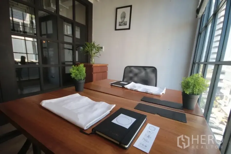 Office Space for rent in Khlong Toei, Bangkok - Sunlit worktable by floor-to-ceiling windows with potted plants and a city outlook.