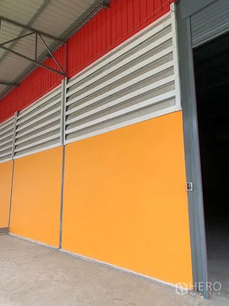 Warehouse for rent or sale in Sai Noi, Nonthaburi - Colorful warehouse facade with orange panels, louvered vents, and an open roller door in Sai Noi, Nonthaburi.