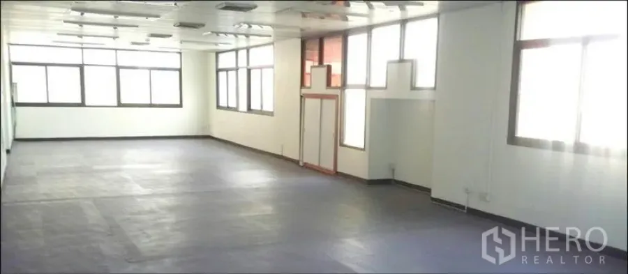 Office Space for rent in Chatuchak, Bangkok - Spacious open-plan office interior in Chatuchak, Bangkok with large windows, white walls, suspended ceiling lights and dark resilient flooring.
