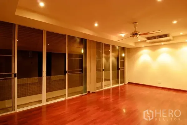 Detached House for rent in Watthana, Bangkok - Spacious living room with polished wood floors, recessed lighting, a ceiling fan and sliding glass doors.