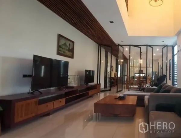 Detached House for sale in Pak Kret, Nonthaburi - Open-plan living room with long wooden TV console, glossy floors and glass partitions.