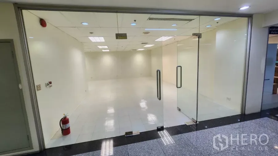 Office Space for rent in Watthana, Bangkok - Open-plan 76 sqm office with glass double doors, white tile flooring, and a fire extinguisher at the entry.