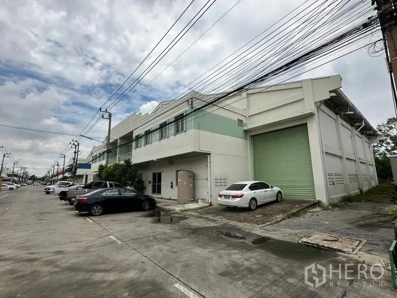 工厂 出租在Khlong Luang, Pathum Thani - 工业区内两层工厂外观，配大型绿色卷帘装卸门与前方停车位。