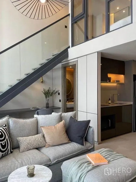 Condominium for rent in Pathum Wan, Bangkok - Cozy lounge facing a kitchenette, staircase with glass balustrade and a doorway leading to a modern bathroom.