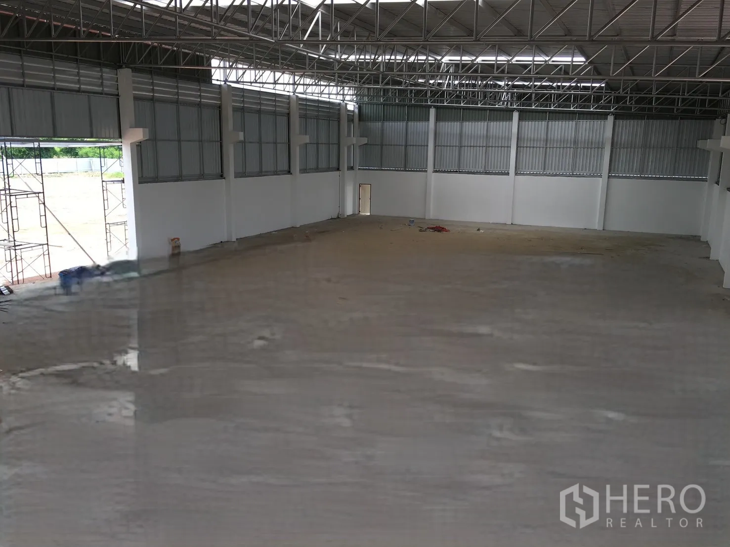 Warehouse for sale in Sai Noi, Nonthaburi - Open-plan warehouse interior showing a concrete floor, steel truss roof, and a wide loading door.