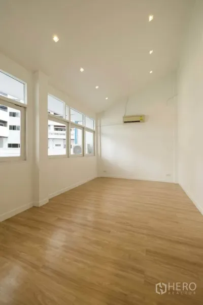 Townhouse for rent in Khlong Toei, Bangkok - Spacious upper-floor room with high ceiling, recessed lights and multiple windows for natural light.