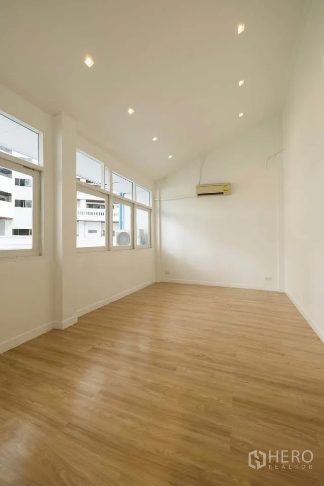 Townhouse for rent in Khlong Toei, Bangkok - Spacious upper-floor room with high ceiling, recessed lights and multiple windows for natural light.