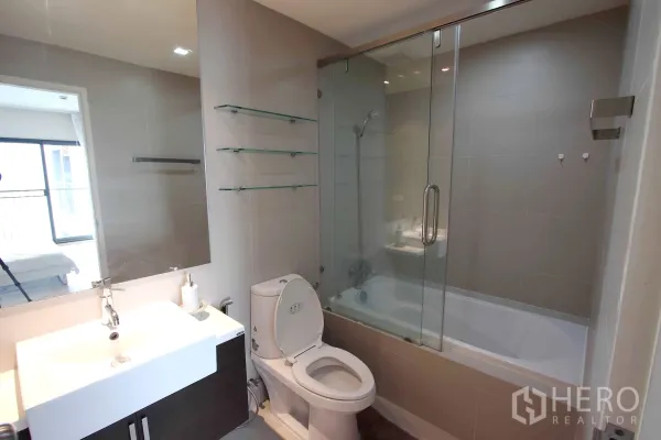 Condominium for rent in Khlong Toei, Bangkok - Contemporary bathroom featuring a wide vanity, toilet and bathtub with a glass shower screen.