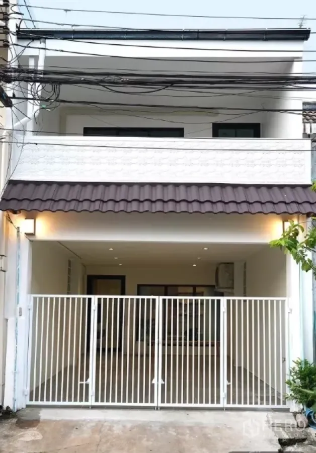 Townhouse for rent in Huai Khwang, Bangkok - Two-storey white townhouse facade with balcony and gated carport in Huai Khwang, Bangkok.