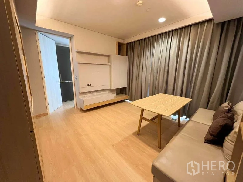 Condominium for rent or sale - Living room with taupe sofa, coffee table, media wall, and blackout curtains.