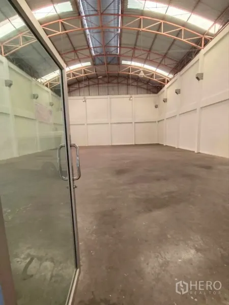 Factory for rent in Phra Samut Chedi, Samut Prakan - Entrance through a glass door into a high-ceiling warehouse with steel truss roof and concrete floor.