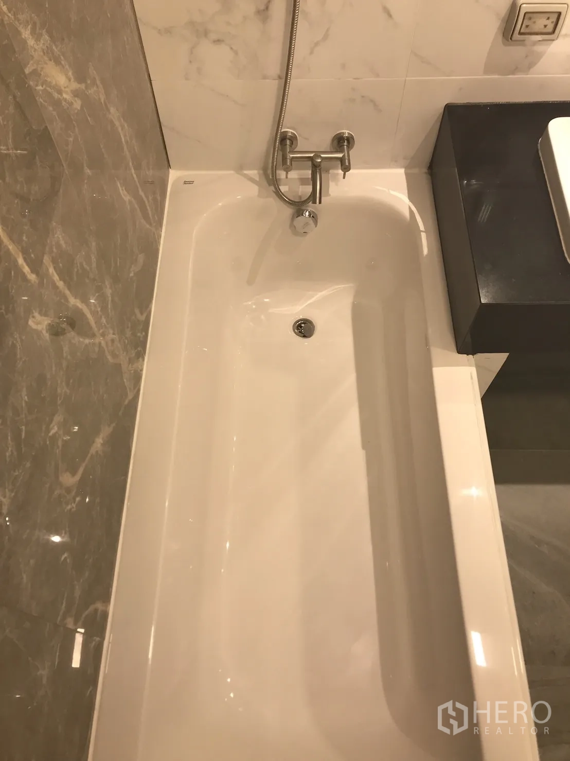 Condominium for rent or sale in Khlong Toei, Bangkok - Close-up of white bathtub with wall-mounted faucet in a marble-clad bathroom.
