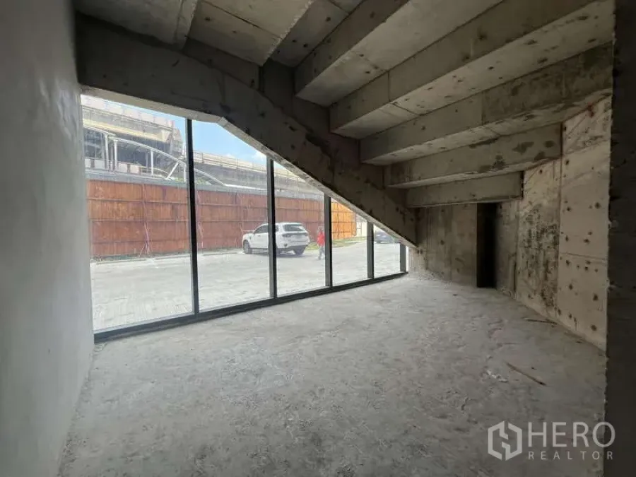 Retail Space for rent - Street-facing retail shell with floor-to-ceiling glass storefront and raw concrete under a sloped ceiling.