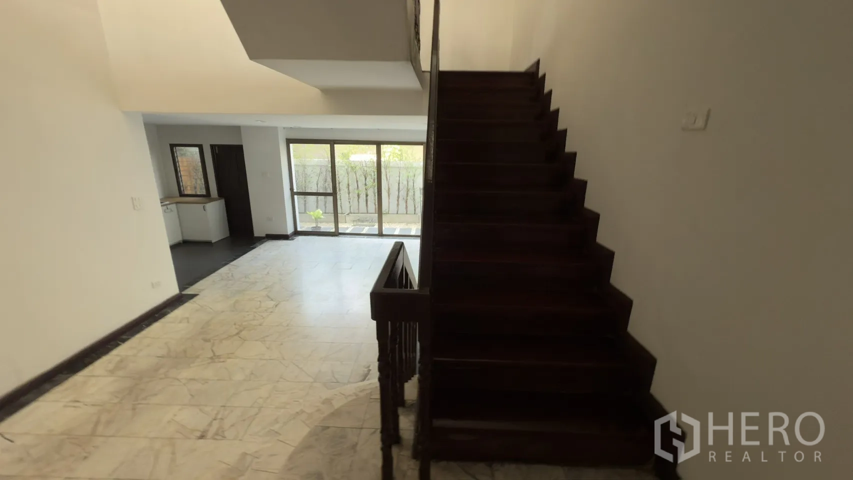 Townhouse for rent in Watthana, Bangkok - Ground-floor living area with marble floors, wooden staircase, and garden-facing glass doors.