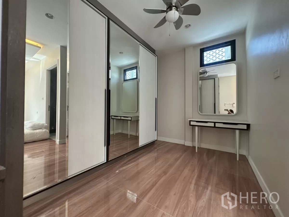 Townhouse for rent in Watthana, Bangkok - Bedroom with mirrored wardrobes, vanity table, and warm wood flooring.