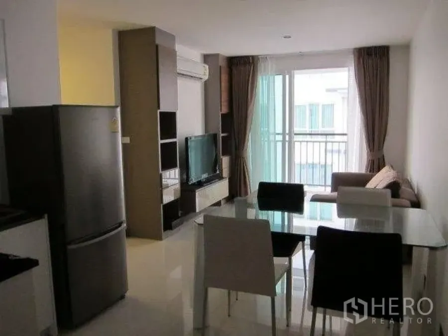 Condominium for rent in Khlong Toei, Bangkok - Open-plan living and dining area with a glass table, TV console, and sliding doors to a balcony bringing in natural light.
