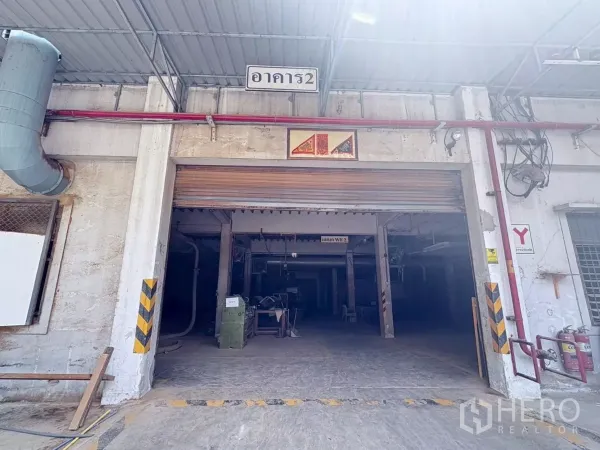 Factory for rent or sale in Bang Khun Thian, Bangkok - Close view of a factory entrance with a metal roller door, safety markings and roof canopy.