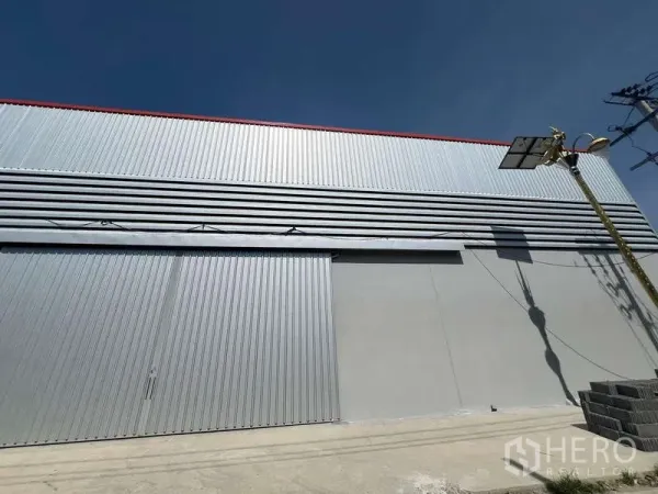 Warehouse for rent in Prawet, Bangkok - Large sliding metal doors and vented facade on the warehouse exterior under clear sky.