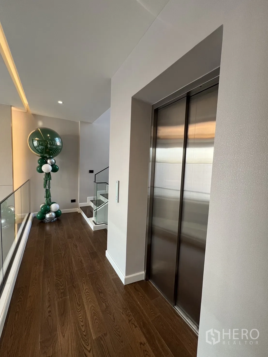 Detached House for sale in Lat Phrao, Bangkok - Upper hallway with home elevator and glass stair railing on wooden flooring.