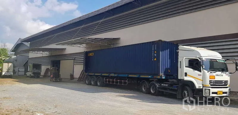 Warehouse for rent in Sam Phran, Nakhon Pathom - Large warehouse exterior with covered loading bay and a 40-foot container truck parked for loading.