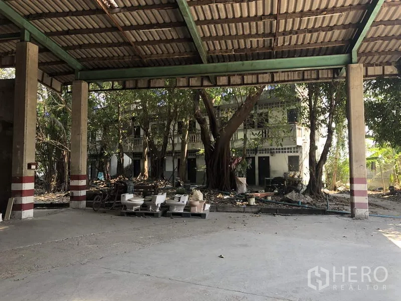 Warehouse for rent in Thanyaburi, Pathum Thani - Covered loading area opening to a courtyard with mature trees and a low-rise building.