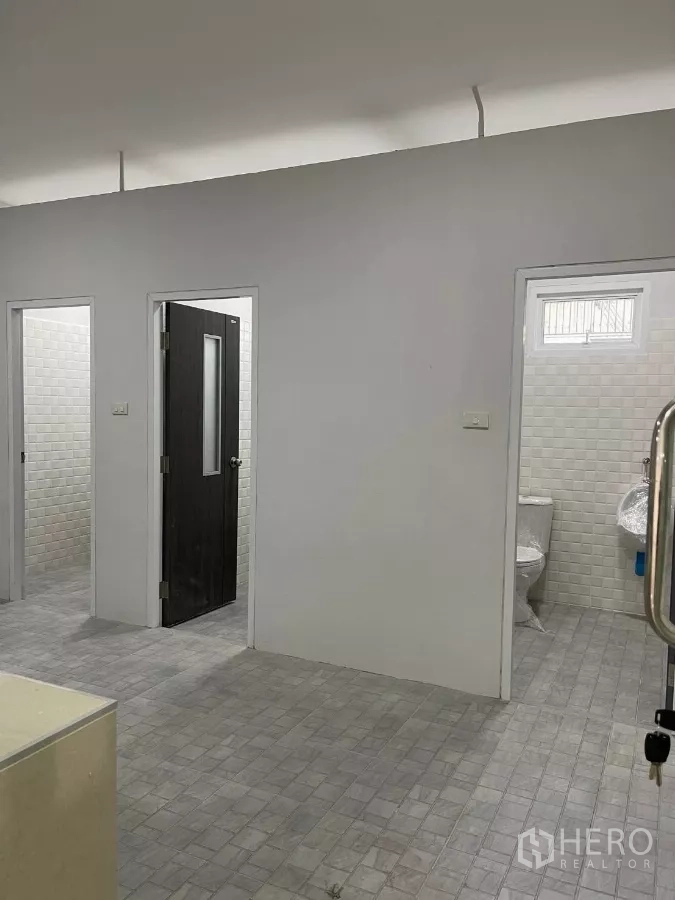Factory for rent or sale in Bang Phli, Samut Prakan - Interior restroom corridor with multiple toilet cubicles and light grey floor tiles.