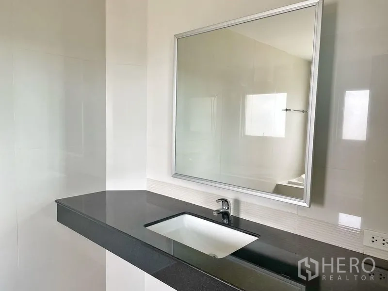 Condominium for rent in Khlong Toei, Bangkok - Modern bathroom vanity with large mirror and under-mount sink on a black countertop.