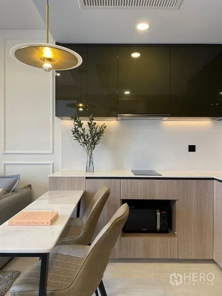 Condominium for rent in Pathum Wan, Bangkok - Modern kitchenette with glossy cabinets, induction hob and a dining counter for two.