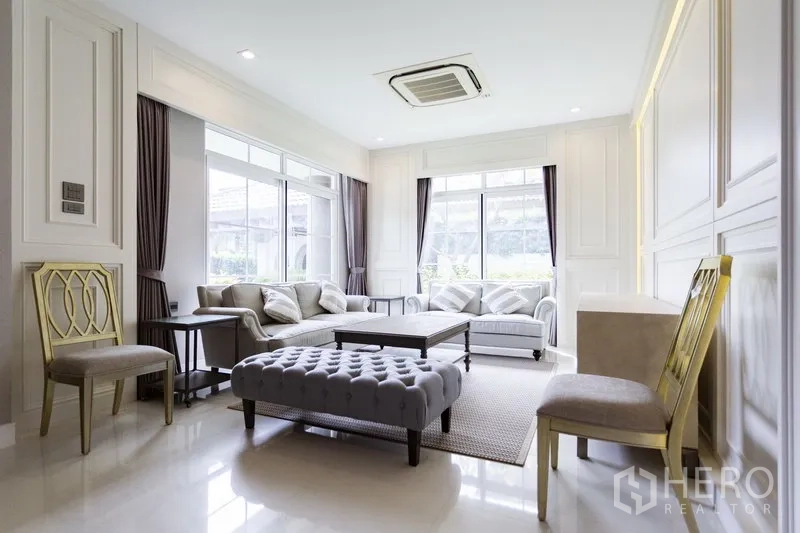 Detached House for rent in Mueang Samut Prakan, Samut Prakan - Bright living room with large windows, neutral decor, sofa set and a ceiling cassette air conditioner.