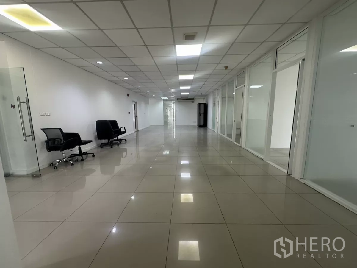 办公空间 出租在Huai Khwang, Bangkok - 长形开放办公区，摆放转椅，沿墙为玻璃办公室与光亮瓷砖地面。