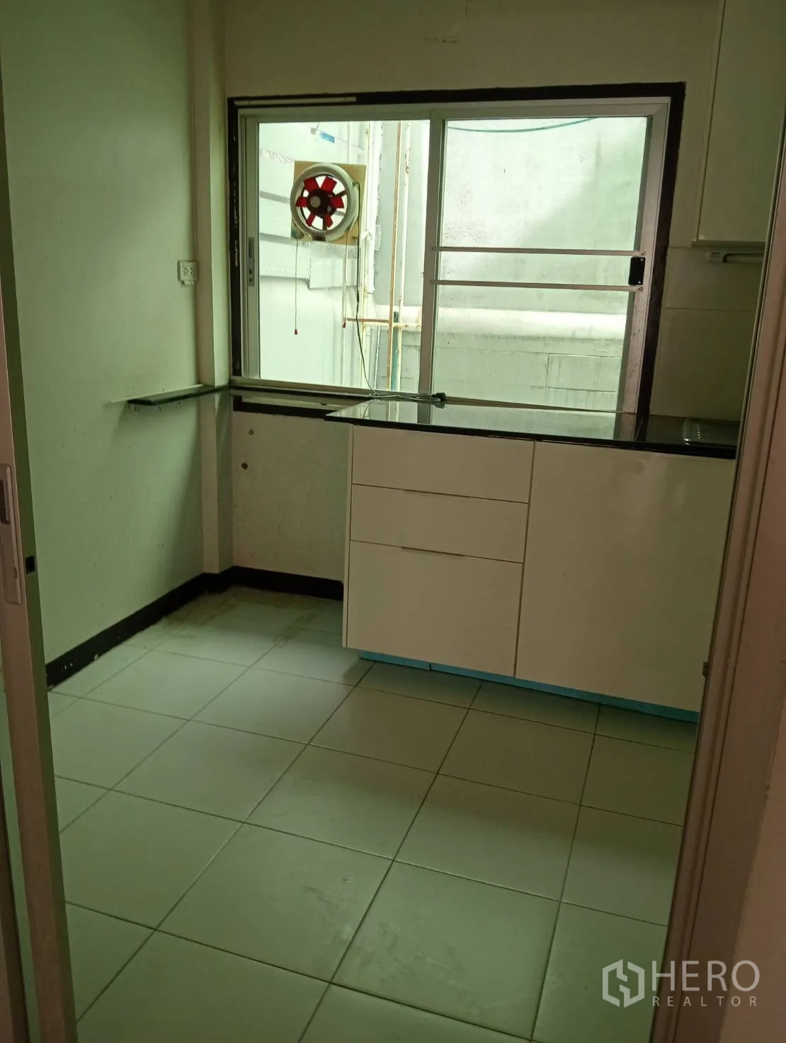 Home Office for rent in Khlong Toei, Bangkok - Kitchen view showing white cabinetry, sliding window and tiled floor.